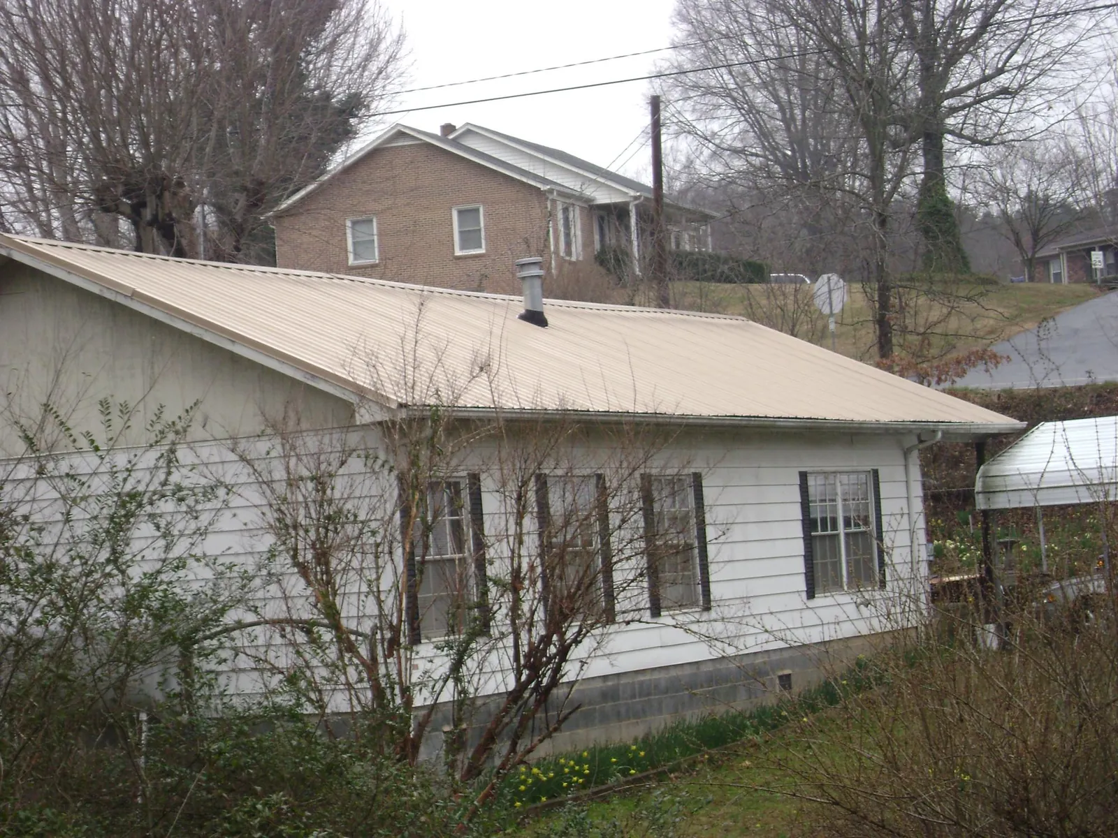 Tan metal roof on a white sided house set into a hillside — Commercial Roofing by Roofing Brothers in Washington Court House